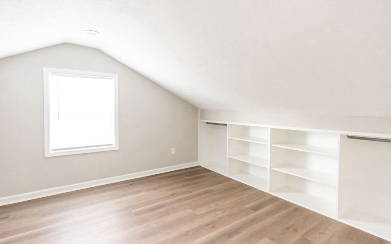 An empty attic bedroom with hardwood floors and white shelves.