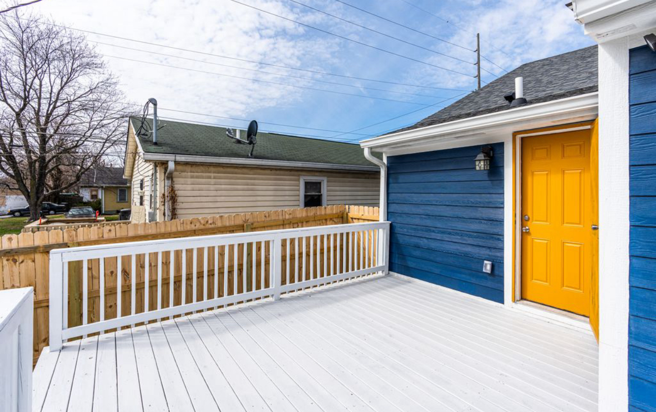 A blue house with a yellow door and a white deck.