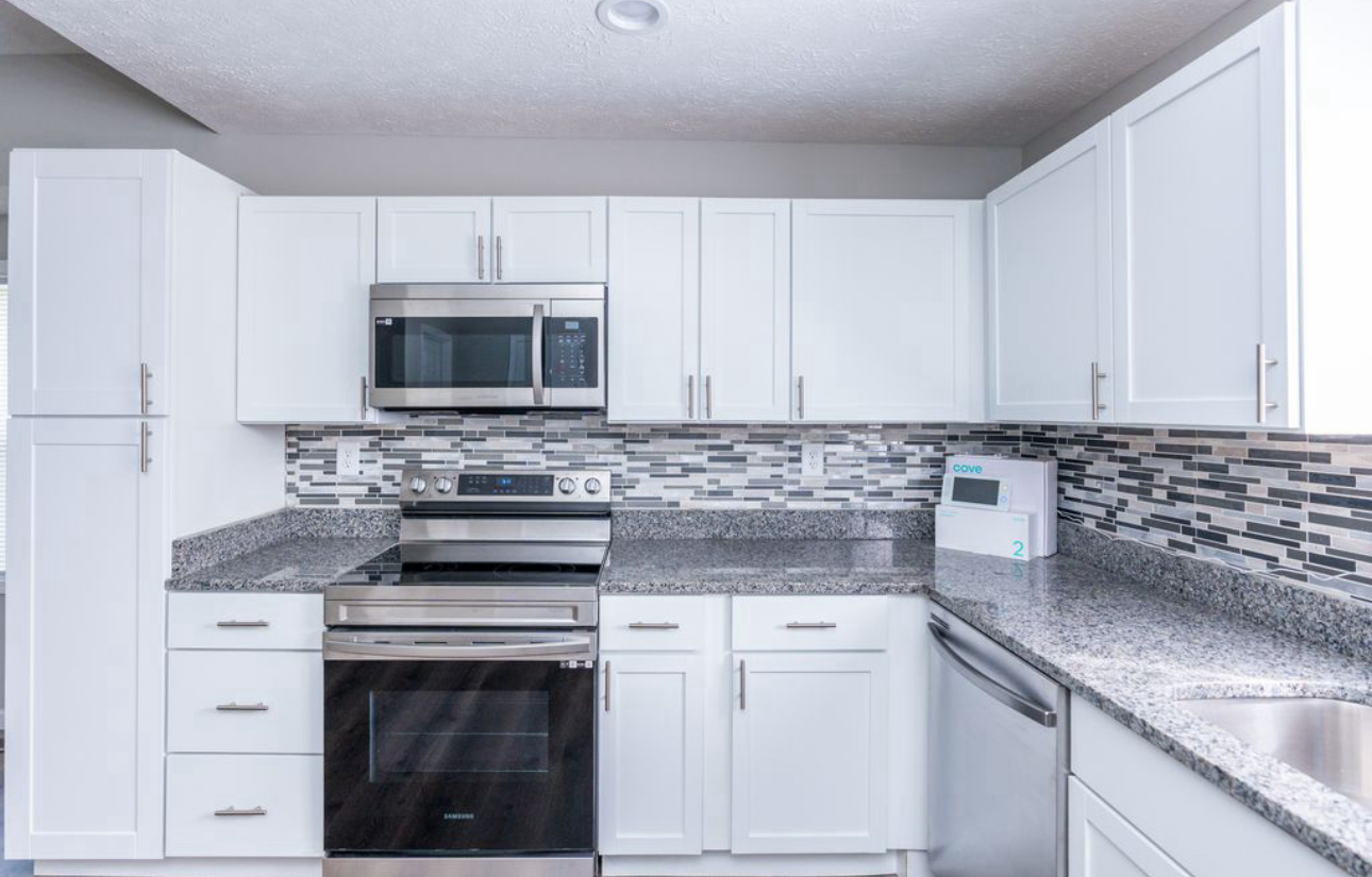 A kitchen with white cabinets , stainless steel appliances , and granite counter tops.