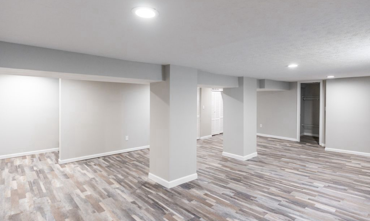 An empty basement with wooden floors and white walls.