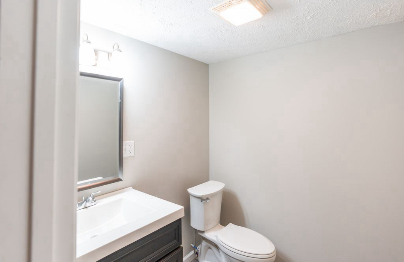 A bathroom with a toilet , sink and mirror.