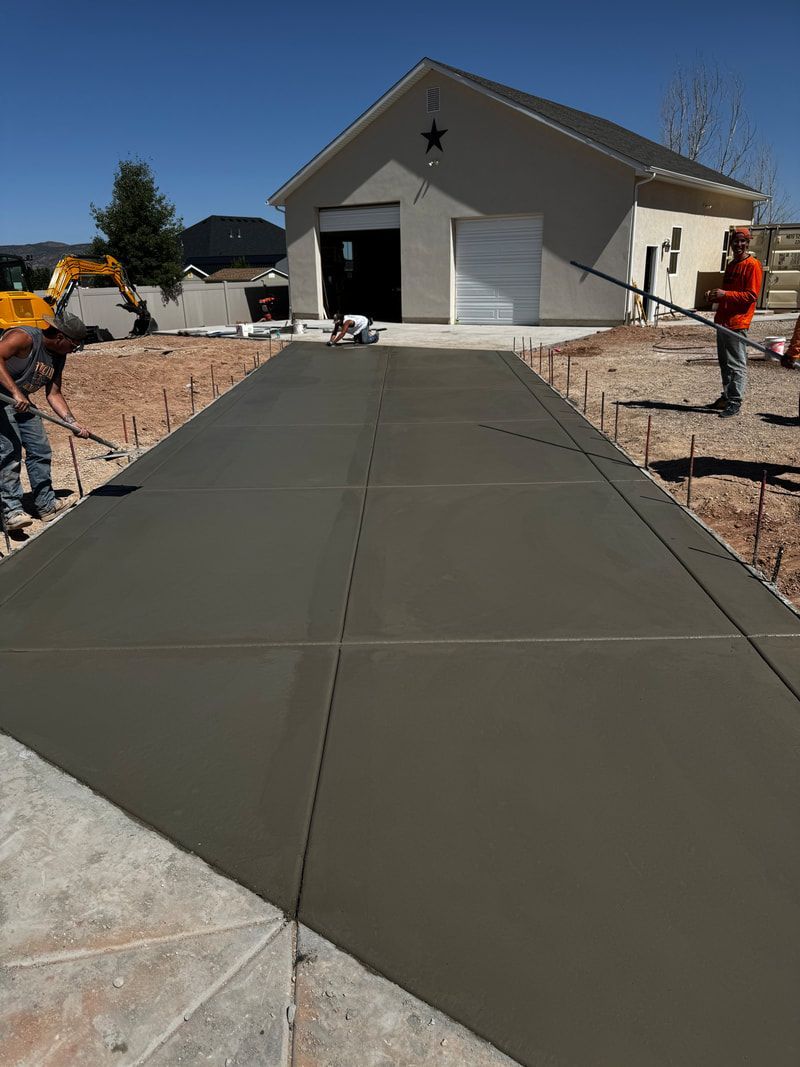 Workers smooth wet concrete on a driveway leading to a garage with a star decoration.
