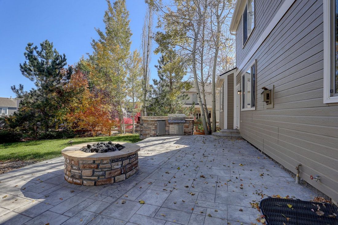 Spacious patio with stone fire pit and outdoor grill surrounded by autumn trees.