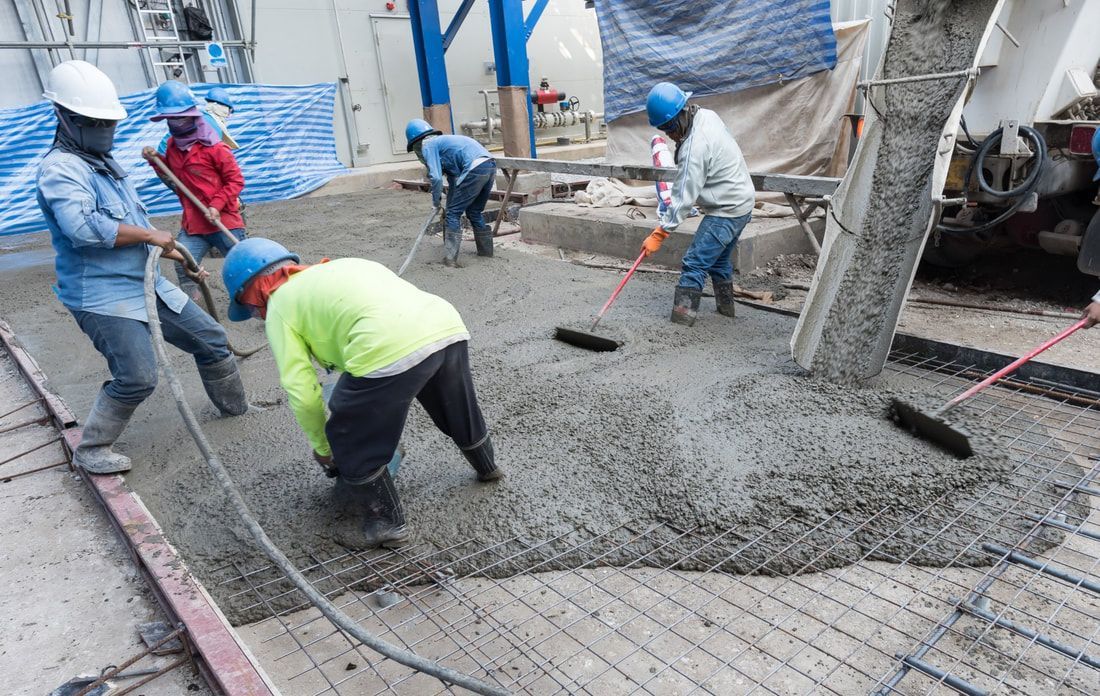 Construction workers in helmets and safety gear smooth freshly poured concrete on a construction site, conveying teamwork.