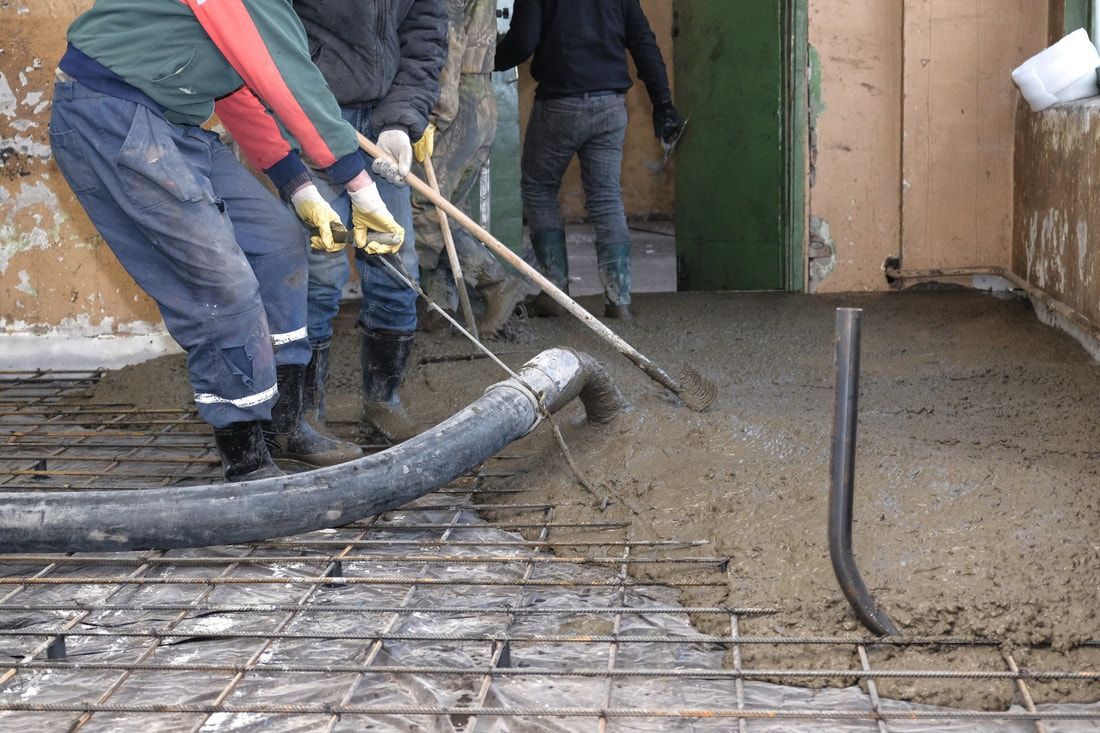 Workers pour concrete over rebar in a construction site. They use tools to spread it evenly. 