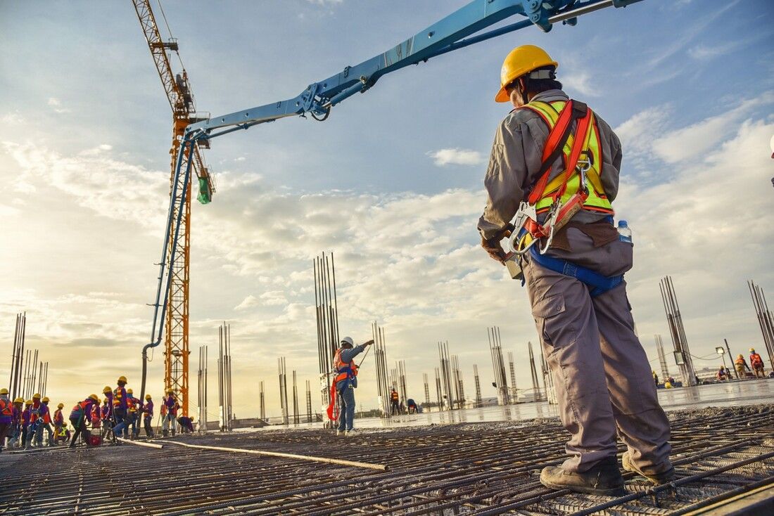 Construction workers on a building site at sunset, wearing safety gear. A crane operates in the background. 