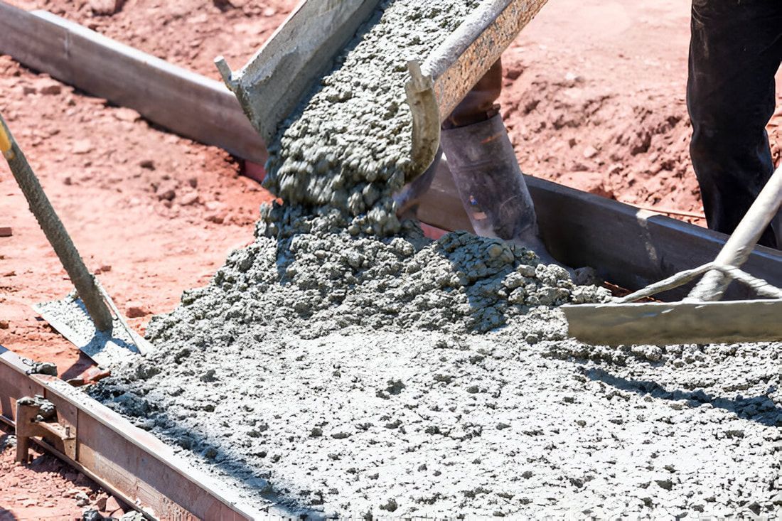 Concrete is poured from a chute into a wooden frame on a construction site.