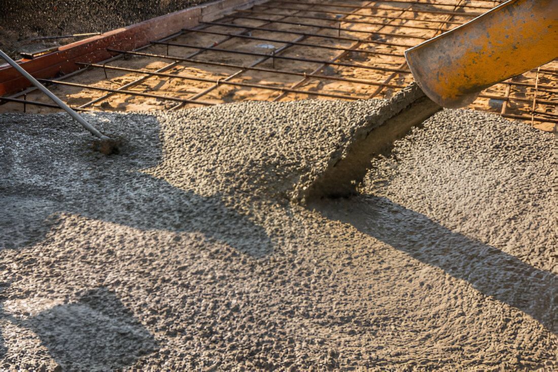 Wet concrete flows from a chute onto steel mesh, forming a textured surface.