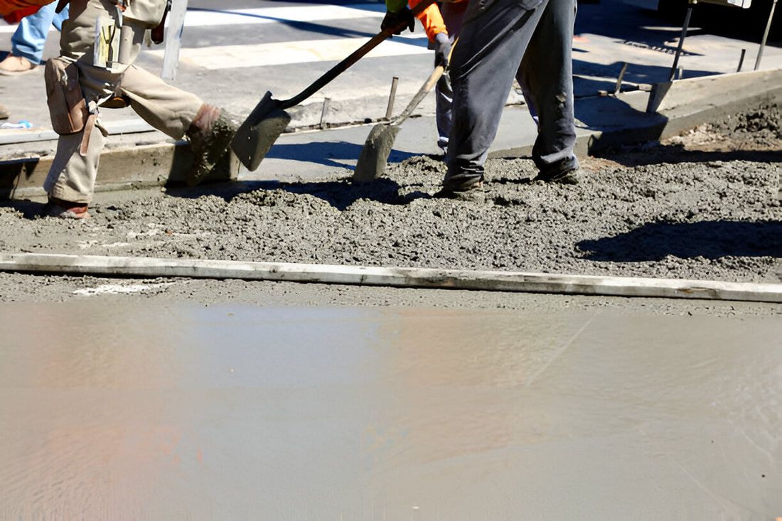 Construction workers in orange safety vests are spreading and smoothing wet concrete at a work site.