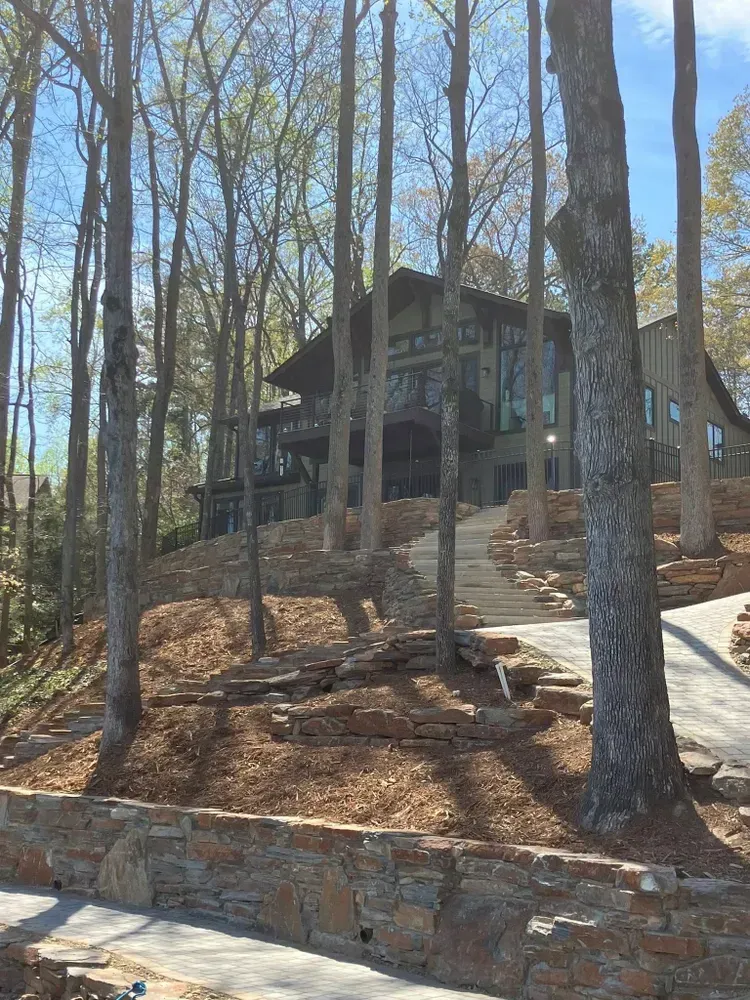 Wooded hillside home with stone steps and retaining wall under tall trees