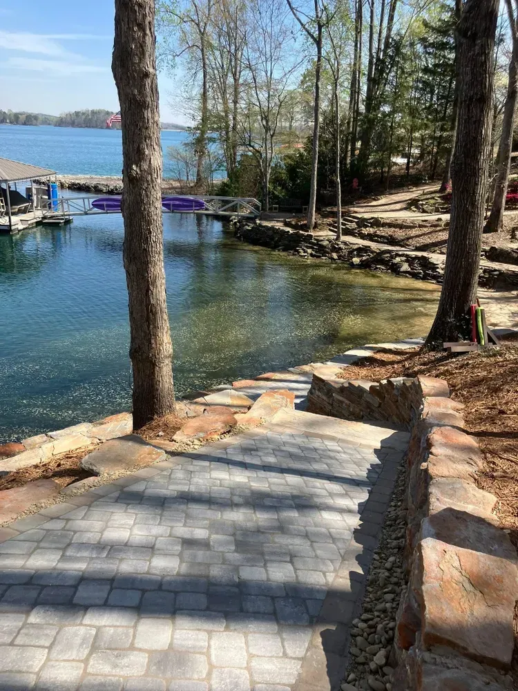 Stone path beside a lake with dock, trees, and rocky shoreline on a sunny day
