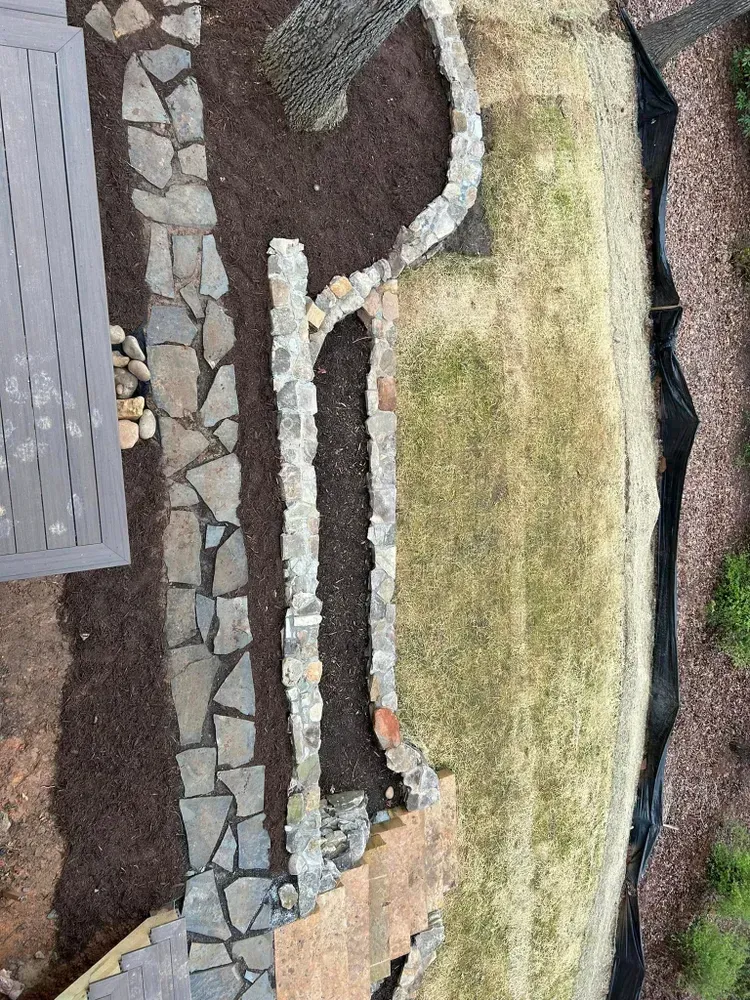 Aerial view of a landscaped rock garden with a stone path, mulch, and green and brown ground cover.