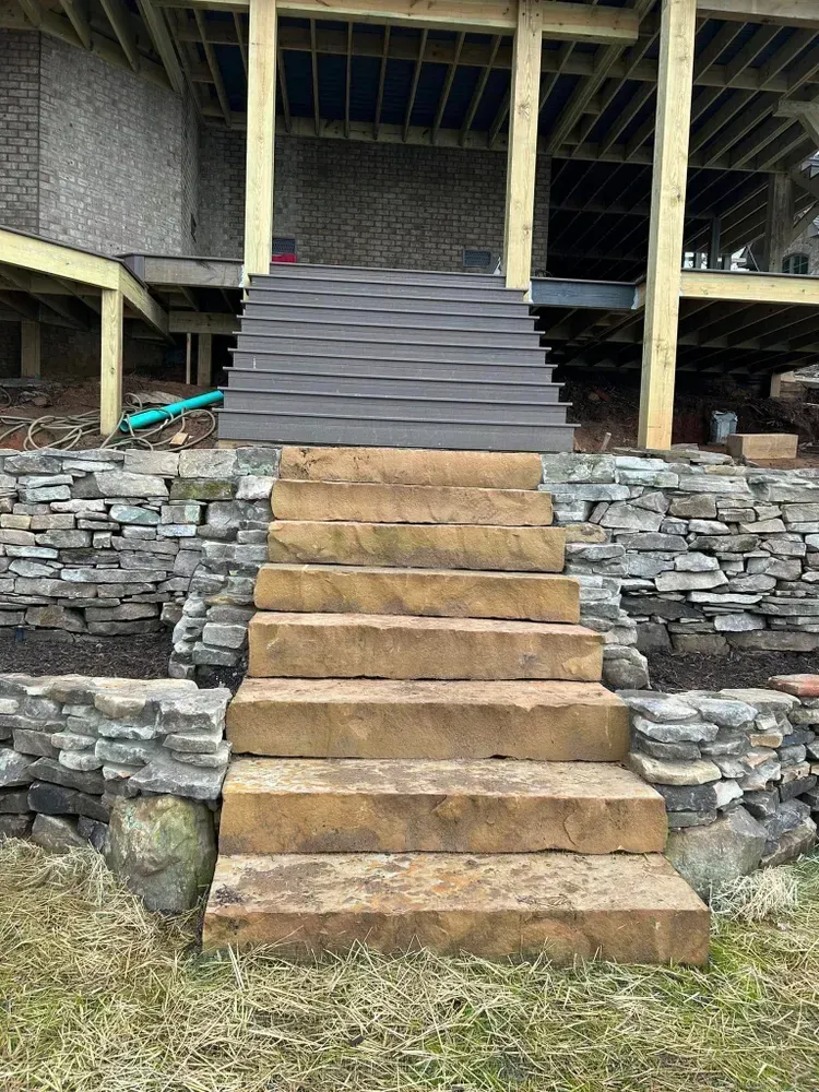 Stone and wooden stairs leading to a raised deck beneath a house.