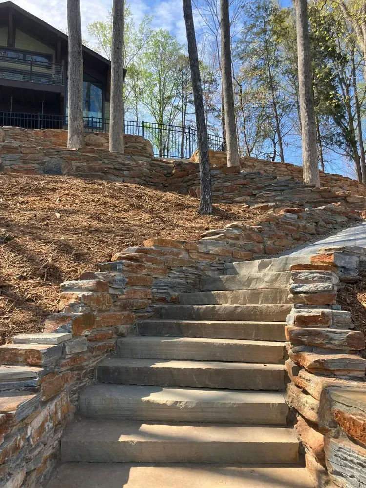 Stone steps climbing a wooded hillside beside a cabin, with dry leaves and bare trees.