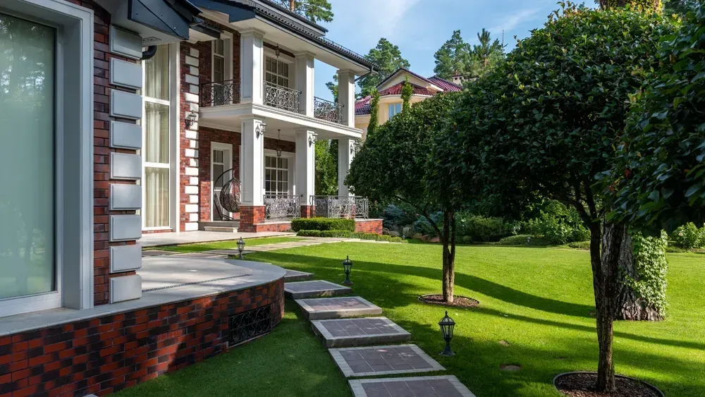 Modern house with a landscaped lawn, stone path, and trimmed trees in bright sunlight