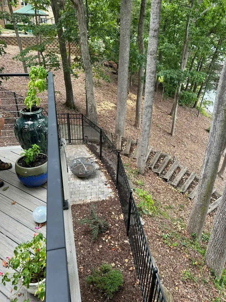 Wooden deck overlooking a wooded hillside with black metal railing and potted plants