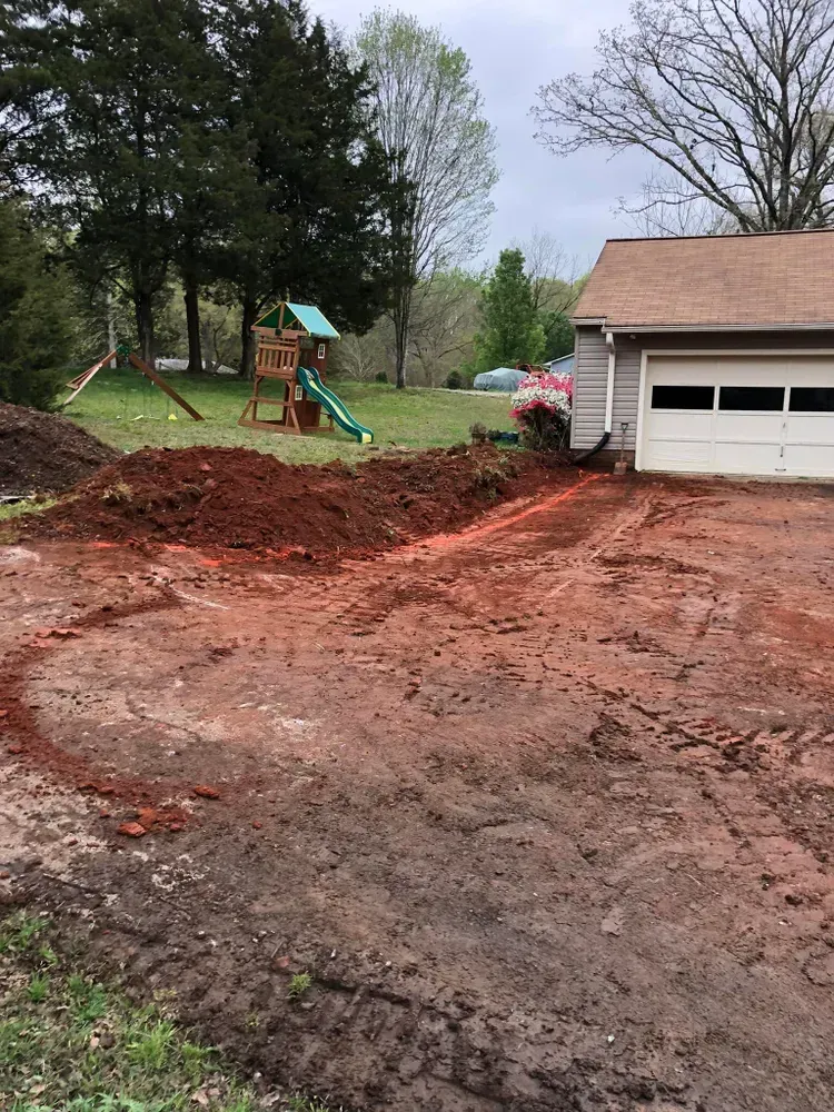 Freshly graded dirt driveway beside a garage, with a red truck and a playground in the yard