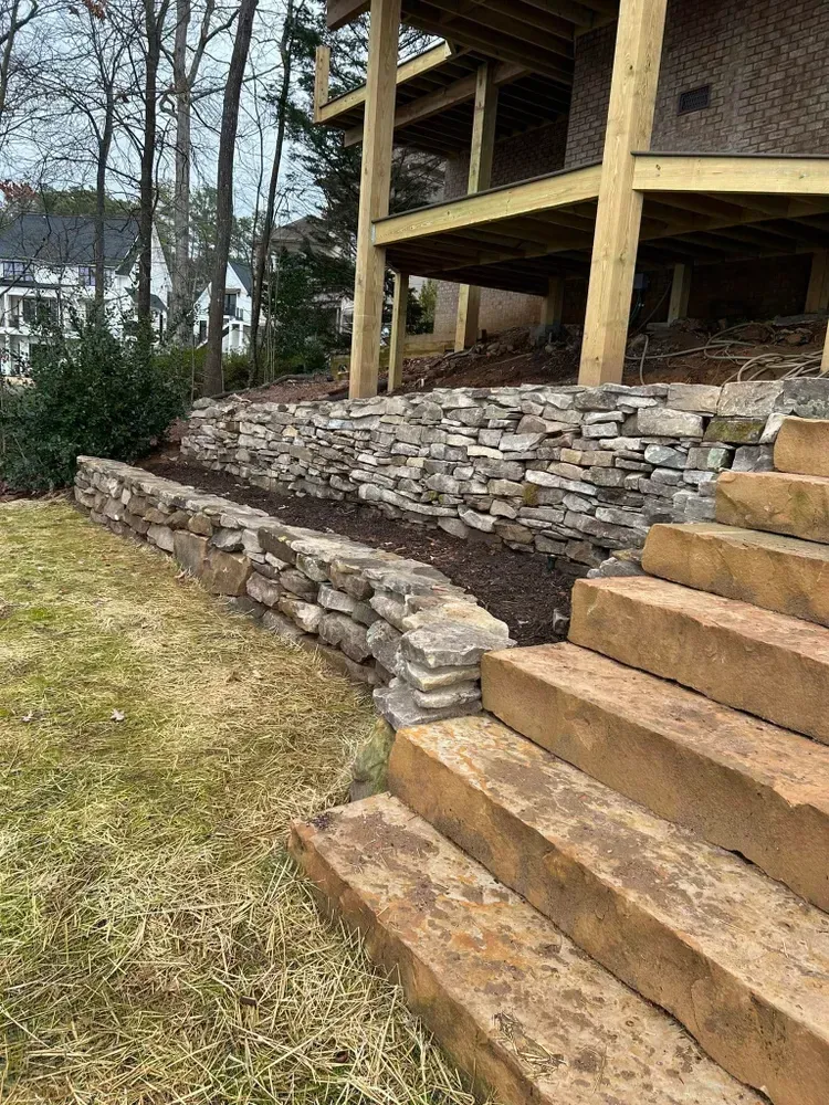Stone retaining wall and wooden steps beside a raised deck in a yard on a cloudy day