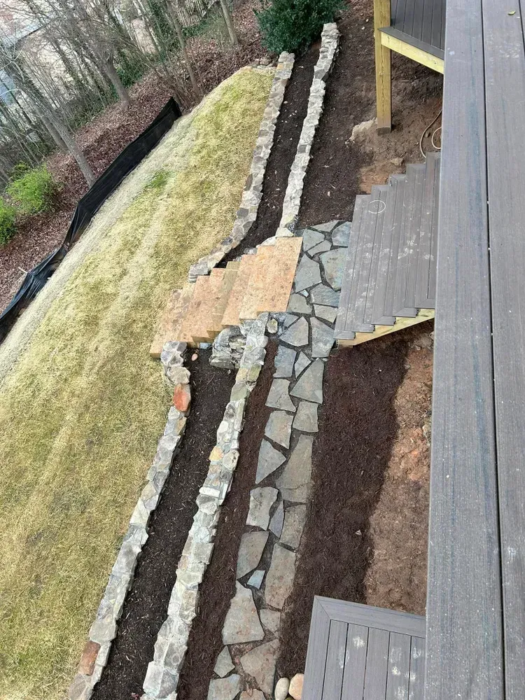 Steep backyard path with stone pavers, bordered by mulch, grass, and a wooden deck