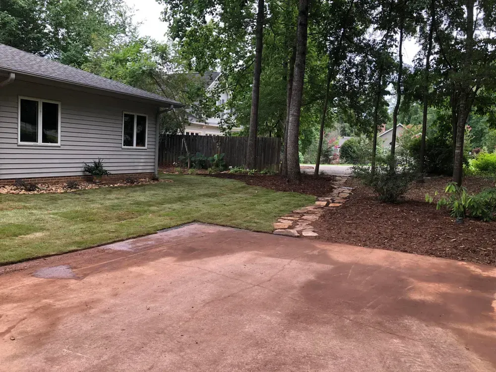 Driveway beside a house, with a lawn, trees, and a stone path leading into the yard.