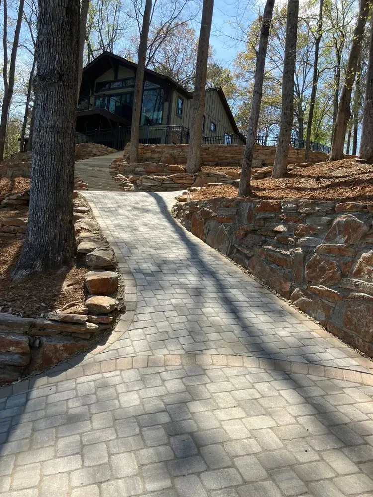Stone walkway leading up to a dark cabin in a wooded hillside setting.