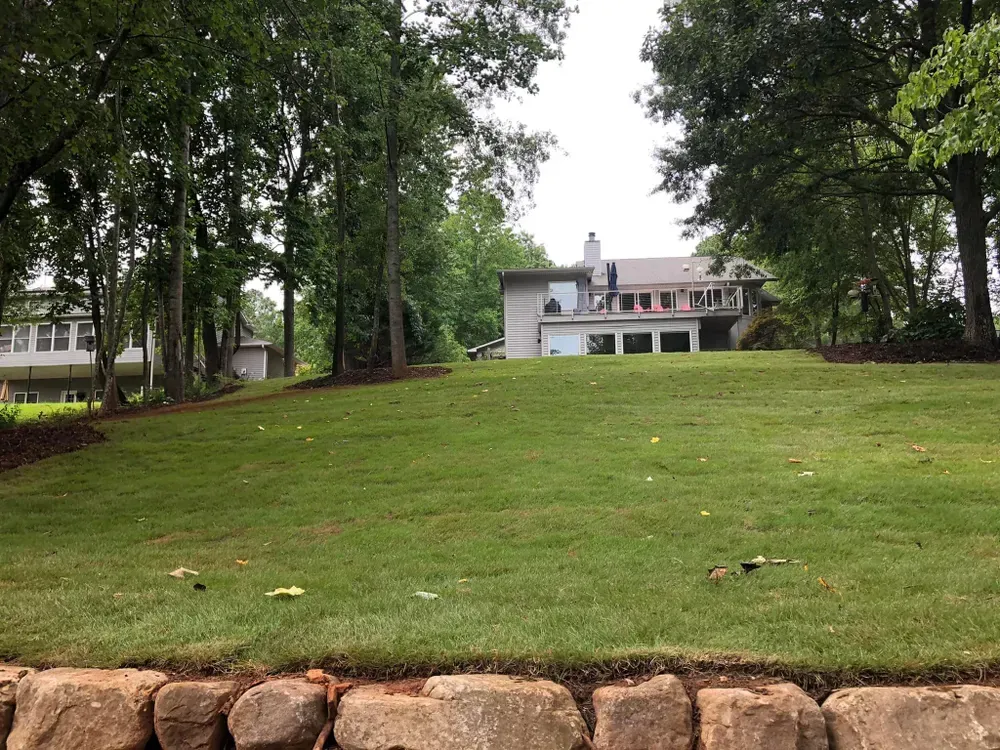 Grassy lawn leading to a white house with trees framing the yard and a stone border in front