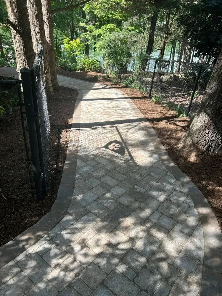 Stone walkway through a wooded park, with sunlight and shadows across the path.