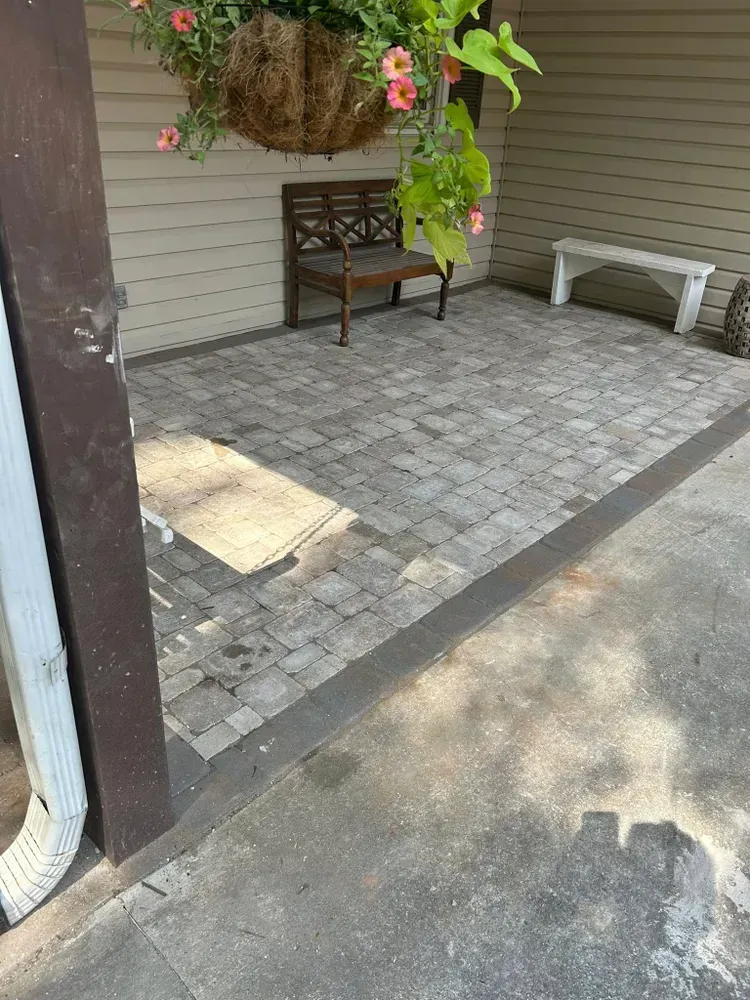 Covered patio with bench, white chair, hanging flowers, and gray paver floor