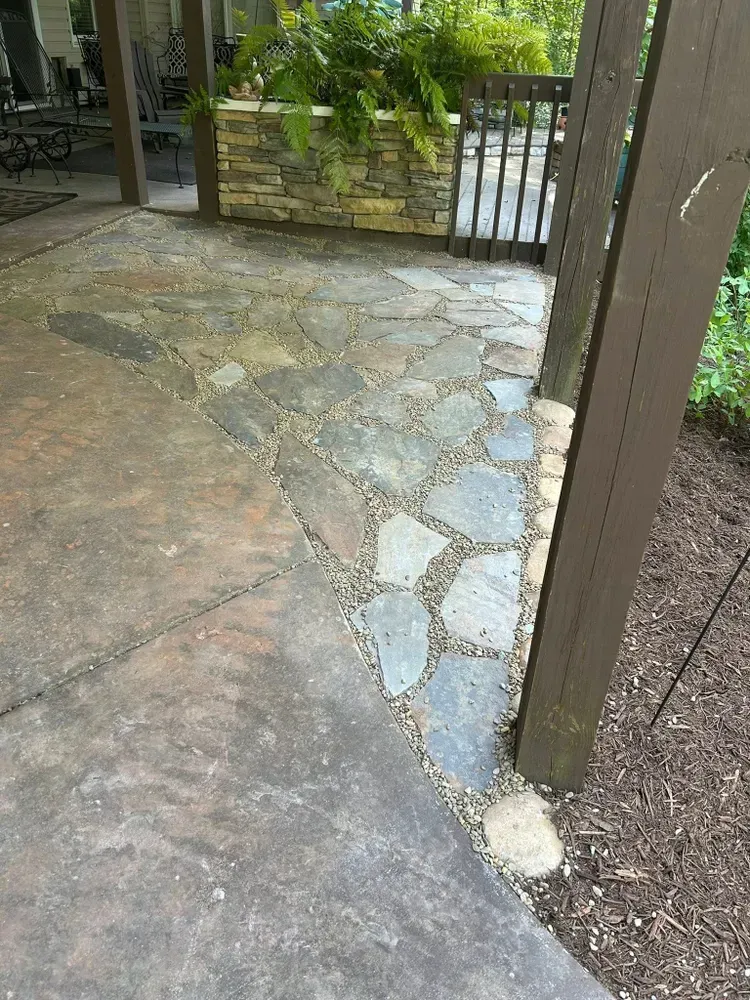 Stone patio with irregular paving and a metal gate beside a pillar, leading to a garden area