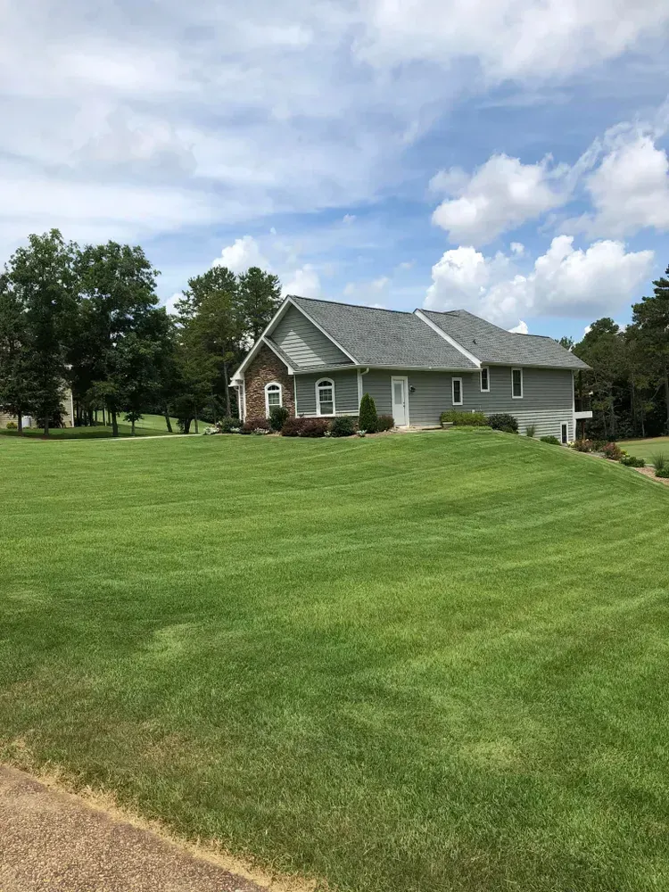 Suburban house with gray roof on a green lawn under a partly cloudy sky