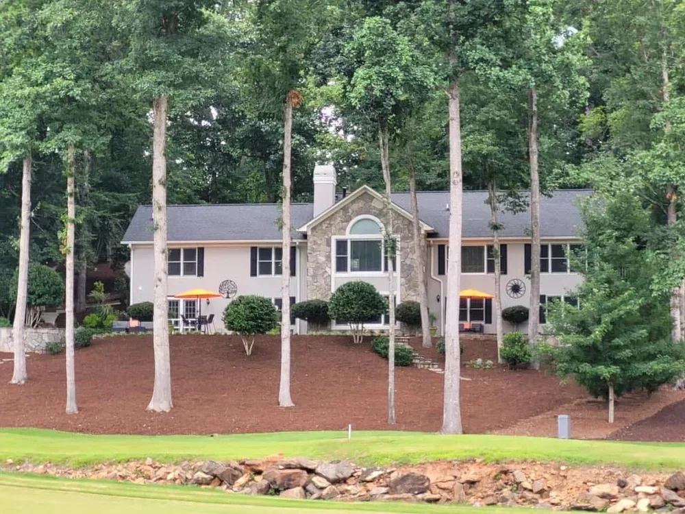 Large beige house with white columns and tall trees on a wooded hillside