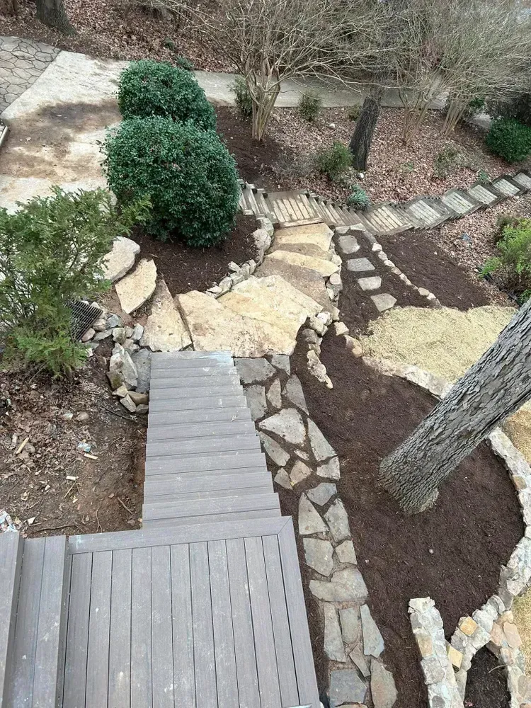 Wooden boardwalk through a landscaped garden with stone paths, shrubs, and mulch beds