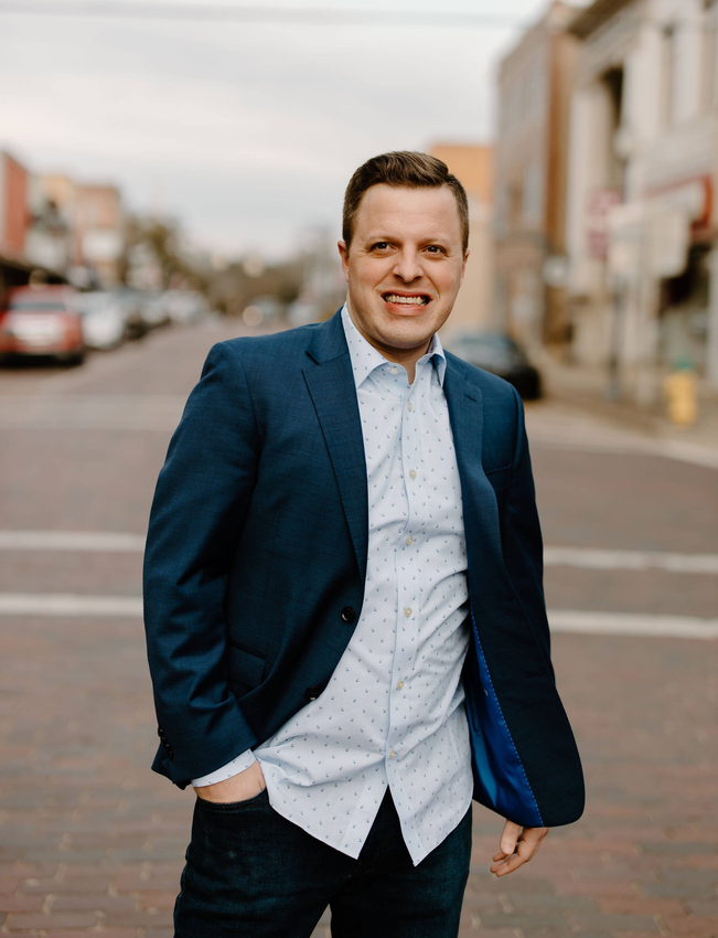 A man in a suit and white shirt is standing on a city street.