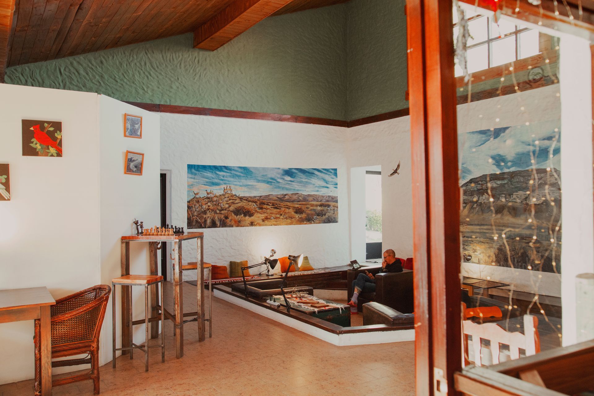 Interior de cafetería con zona de asientos elevada, arte en las paredes y una ventana con luces de colores.