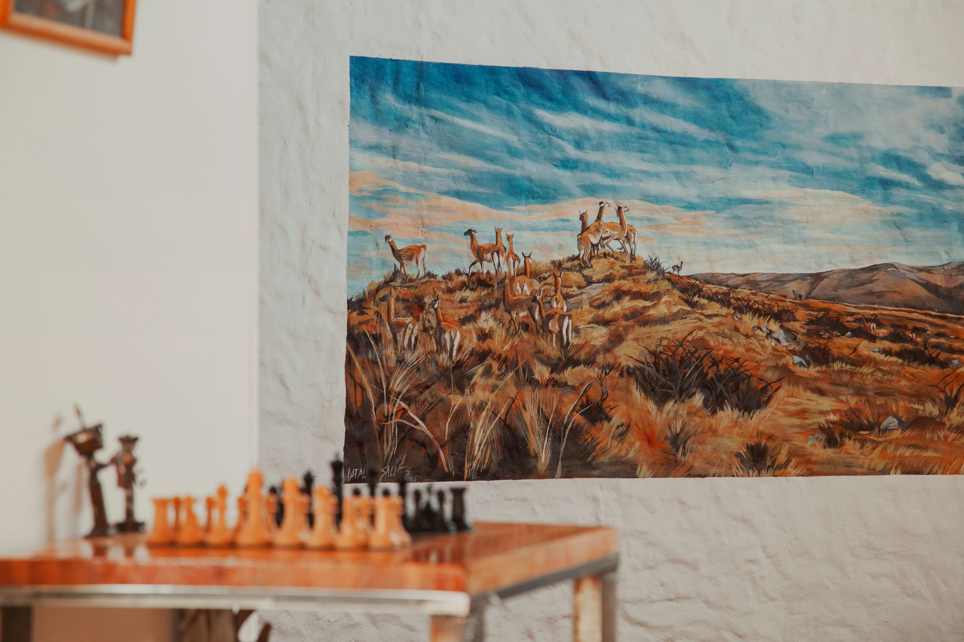 Juego de ajedrez sobre mesa, ilustración de llamas en la ladera, fondo de cielo azul.