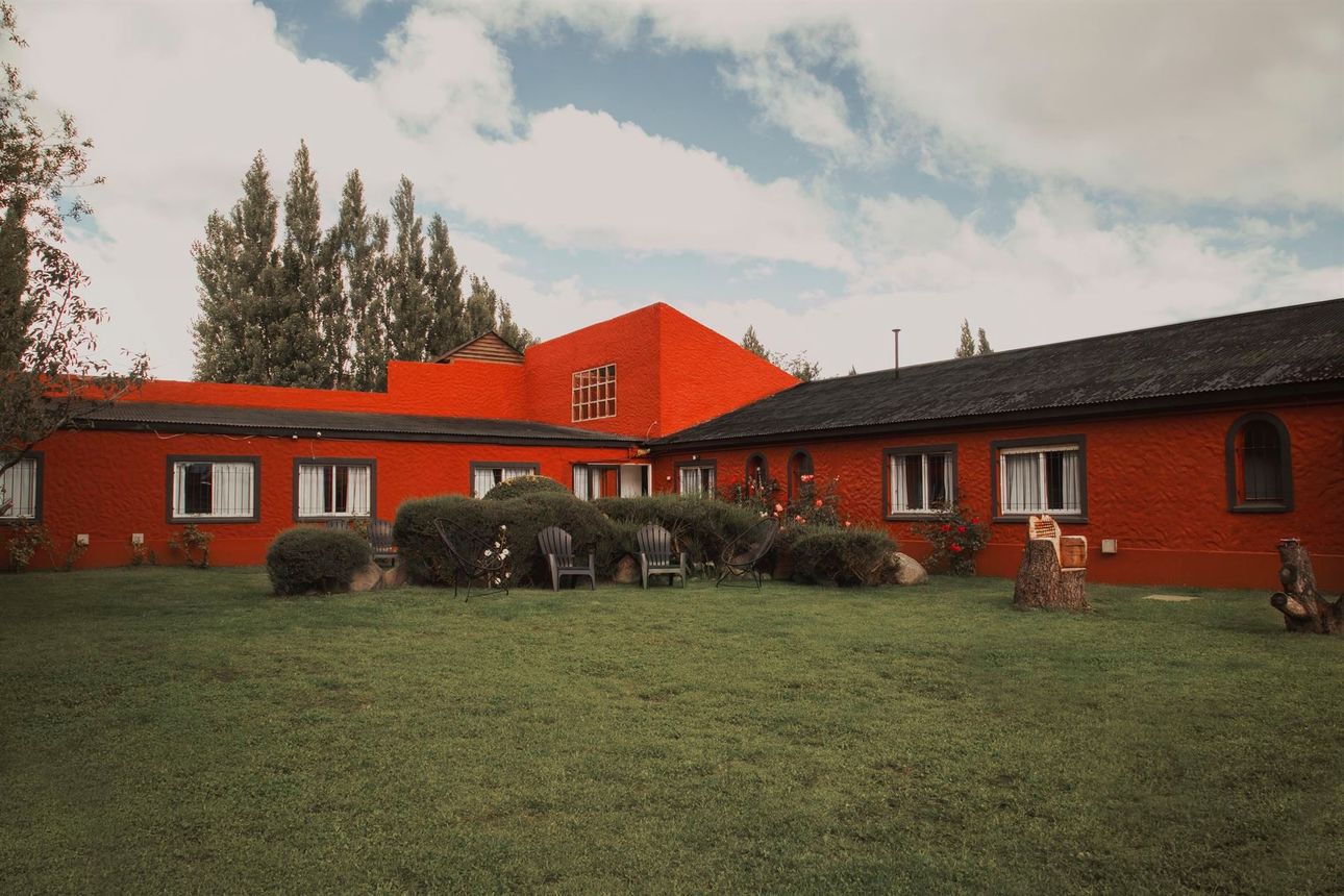 Un gran edificio rojo con techo negro está rodeado de césped y árboles.