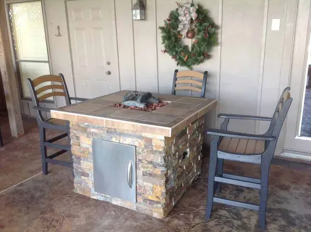 A patio with a fire pit and chairs and a wreath on the wall.