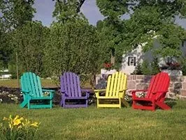 A row of colorful adirondack chairs are sitting on top of a lush green lawn.