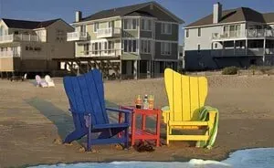 Three lawn chairs are sitting on the beach in front of a house.