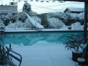 A swimming pool covered in snow with a bird statue in the background