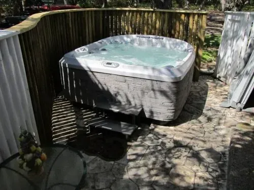 A hot tub is sitting on a patio next to a wooden fence.