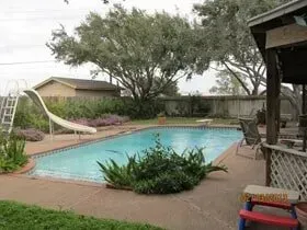 A large swimming pool with a slide in the backyard of a house.