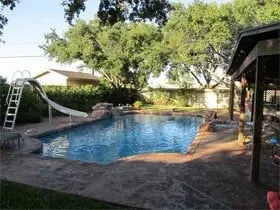 A large swimming pool with a slide in the backyard of a house.