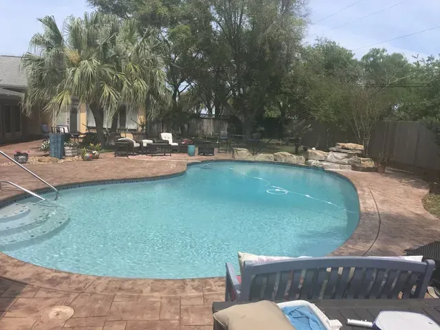 A large swimming pool surrounded by palm trees and a bench.