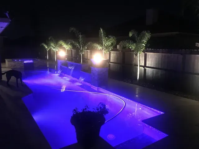 A large swimming pool is lit up at night with purple lights.