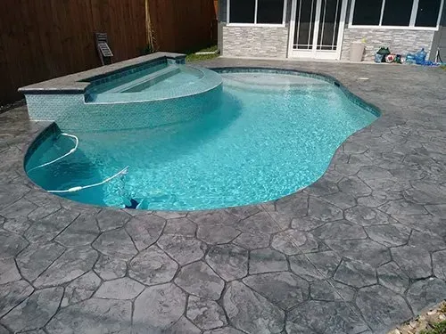 A large swimming pool is surrounded by a stone patio.