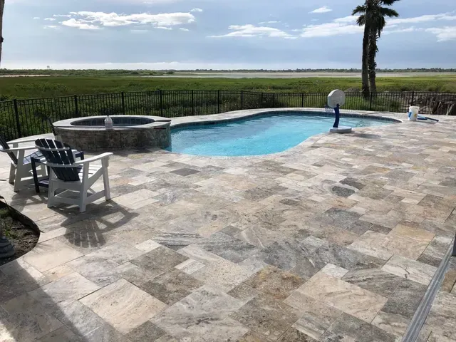 A large swimming pool is surrounded by a tiled patio and chairs.