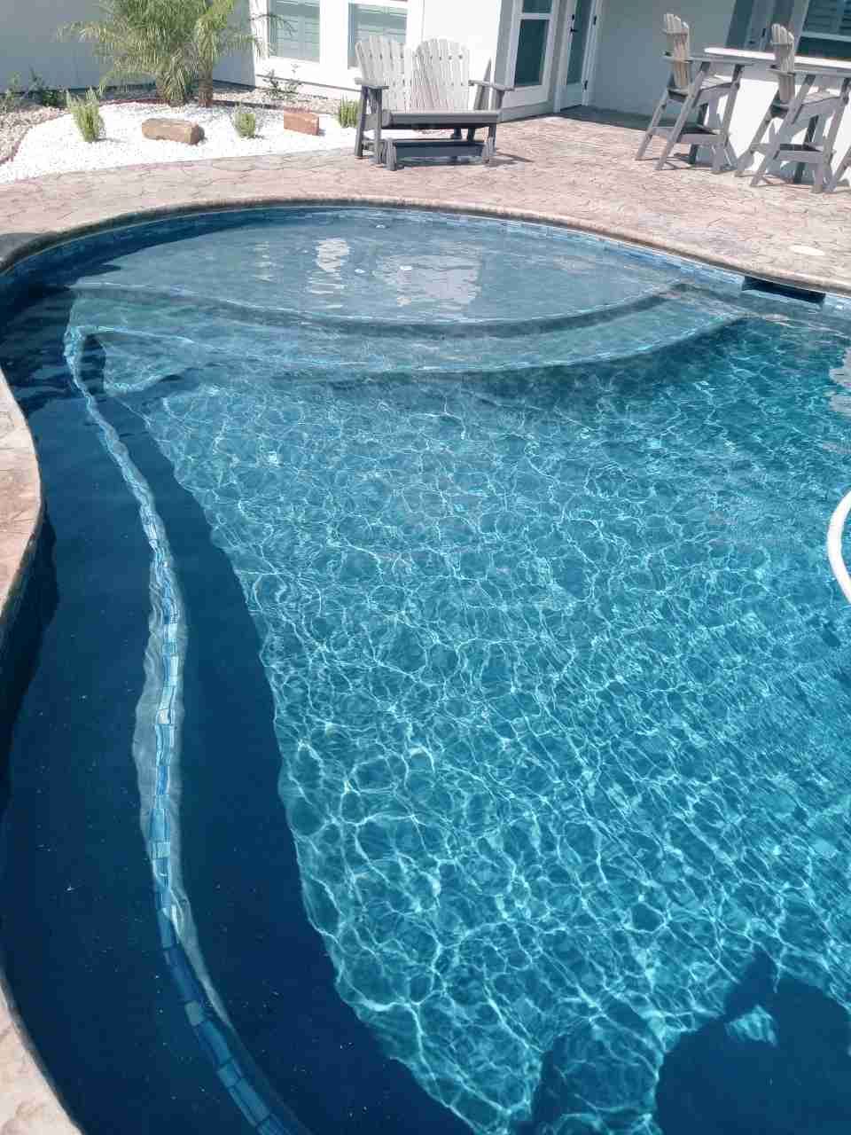 A large swimming pool with stairs and a chair in the background.