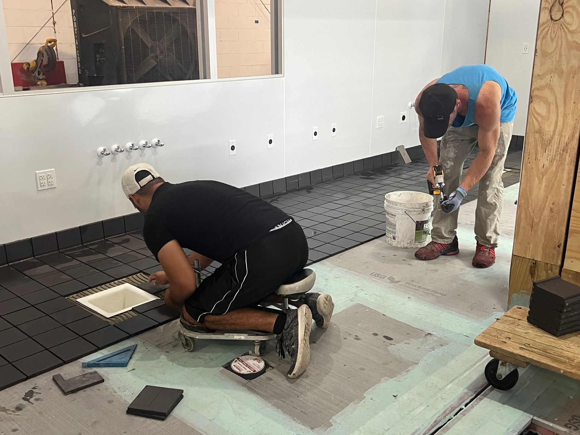 Two men are working on a tile floor in a room