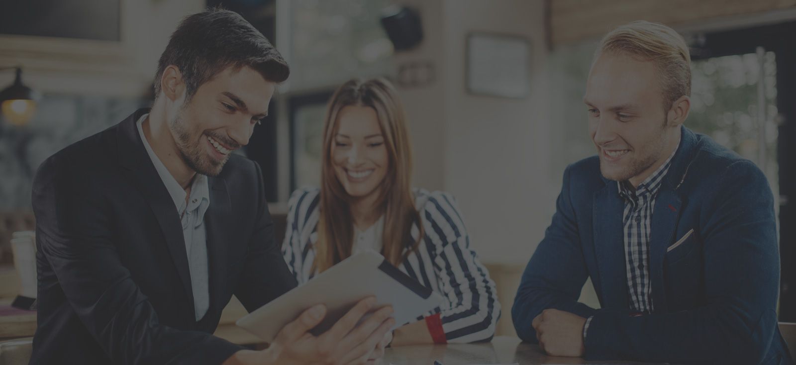 Three people looking at a tablet, smiling, in a casual setting.